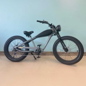 A matte black and gray Revi Silver & Black Cheetah eBike cruiser with large, thick tires is parked indoors against a light blue wall and tan floor.