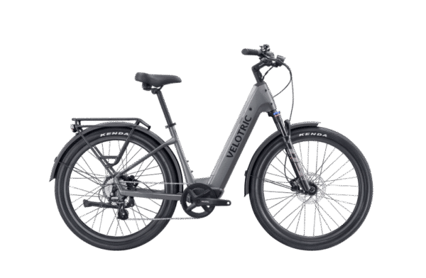 A silver Velotric electric bicycle with a step-through frame, front and rear fenders, rear cargo rack, and thick Kenda tires, shown in profile on a white background.